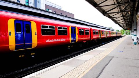 A red South Western Railway train at a station. 