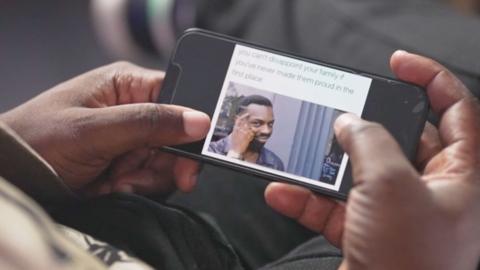 A man's hands holding a phone, with an image of a meme on the screen, showing a man looking at the camera and pointing to his forehead