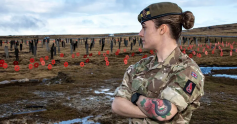 A woman stands in military uniform looking out over a field of remembrance.
