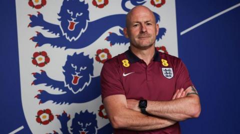 Lee Carsley standing arms folded in front of the England badge