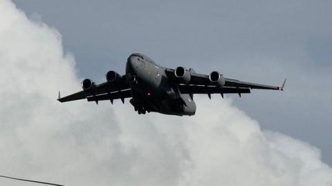 A large grey US Air Force military jet aircraft against a cloudy grey blue sky above a telegraph wire on Prestwick.
