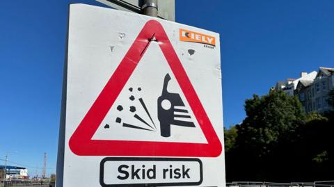 A road sign that has a car on it and the works skid risk.