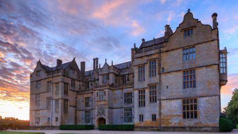 A stately home stands in the dusk, with three floors stretching into the inky, pink sky.