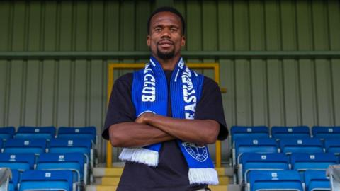 Manny Duku, wearing a blue Eastleigh scarf, poses for a photo at the club's stadium