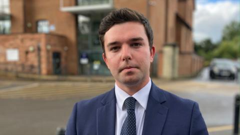 a man with dark hair, blue suit, shirt and tie