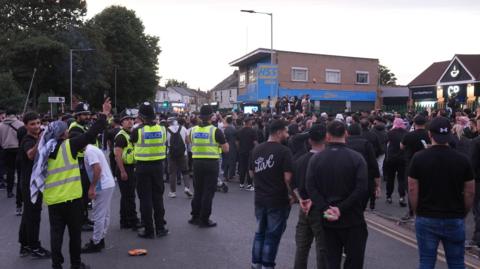 Anti-racism protesters stand in a street with four police officers watching from the back of the crowd