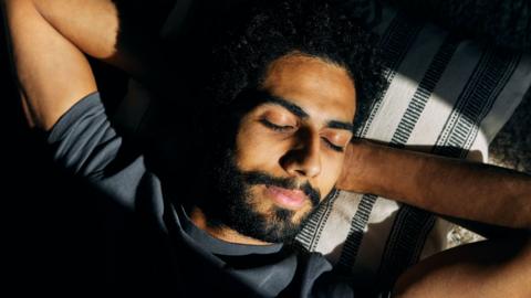 A man sleeps with his hands behind his head.