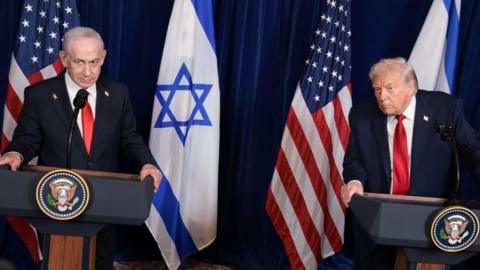 Trump and Netanyahu speaking at a conference, while both wearing suits with red ties with Israeli and US flags in background