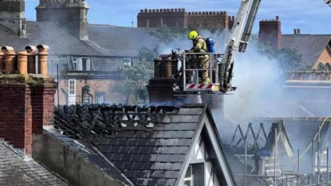 A firefighter attending to damage to the roof of a property in Harrogate while smoke billows around 