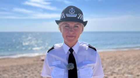 Det Supt Alex Doughty, strategic lead for organised immigration crime at Devon and Cornwall Police, standing on a beach in a police uniform, including hat 