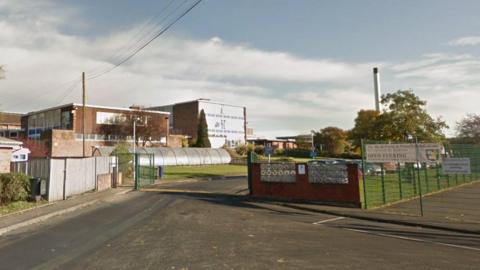The entrance to a school campus with green metal gates and fences