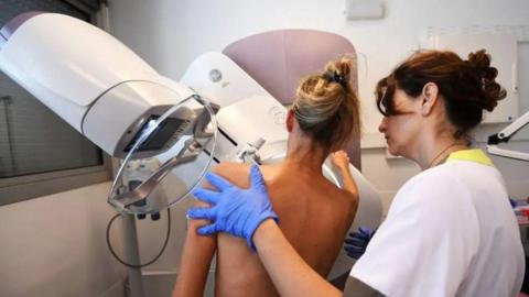 A nurse holding the shoulders of a woman having a mammogram in a clinic