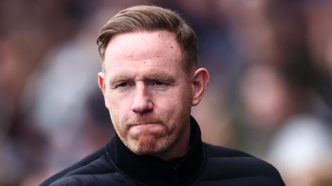 Shrewsbury Town manager Gavin Cowan looks thoughtful wearing warm padded dark blue jacket