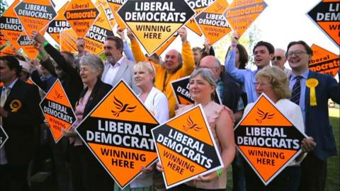 Councillors outside gathered together holding signs saying "Liberal Democrats winning here".
