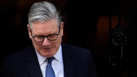 Sir Keir Starmer looks down, with a black background