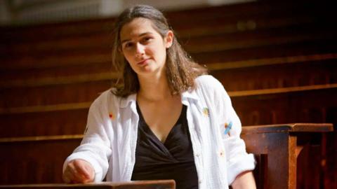 Woman in a white shirt sitting in a wooden lecture theatre

