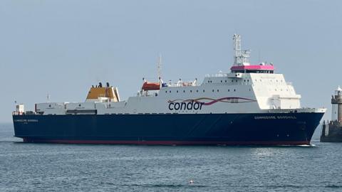 A large commercial vessel, the Commodore Goodwill, heading into a harbour. Skies are blue.
