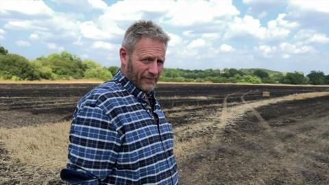 A farmer stands on a field that is charred and scorched from a fire. 