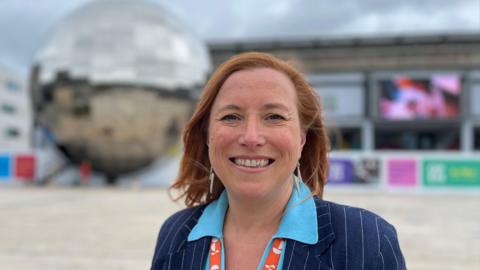 A woman with red hair stood in Millennium Square, a large open space, with the planetarium - a metal dome behind her