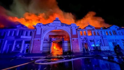 The facade of Odesa's market at nighttime, with a fire raging behind it