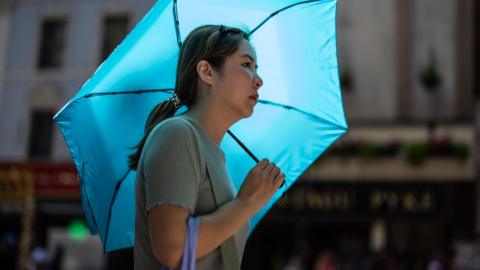 A woman cools herself beneath an umbrella as she walks through central London on June 23, 2026 in London, England. 