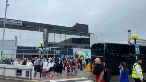 A crowd of people with suitcases standing outside Birmingham Airport 