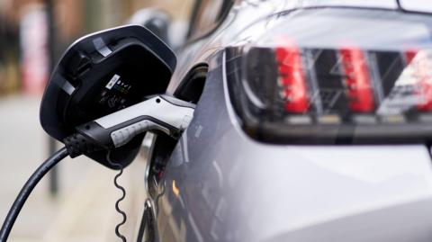 Close-up of an electric car charger plugged into a silver car