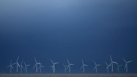 Rhes o 16 o dyrbinau gwynt ar waelod y llun, gyda'r awyr uwchben yn las tywyll