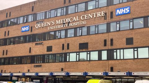 The exterior of the Queen's Medical Centre (QMC) in Nottingham, showing the sign and three rows of windows 