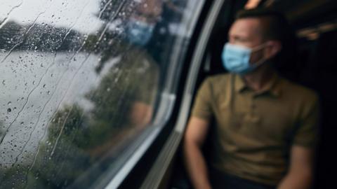 A man in a mask looking through a rainy train window