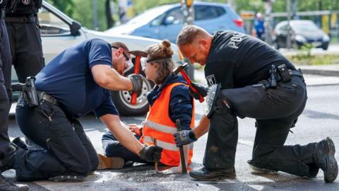 Police officers work to free a Letzte Generation (Last Generation) climate activist after he glued himself to the asphalt during a climate protest in Berlin, Germany, 22 May 2023