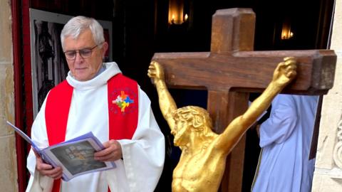 Priest-in-charge Jean-Louise Brunel in background, with crucifix in foreground