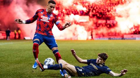 Rangers captain James Tavernier and Dundee player Owen Beck on the pitch as pyrotechnics go off in the background