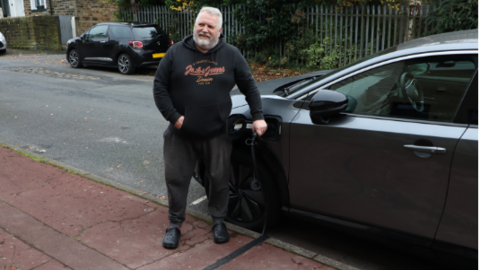 Volunteer motorist Mike Pickering smiles as he charges his car with an electric cable sunken into the pavement