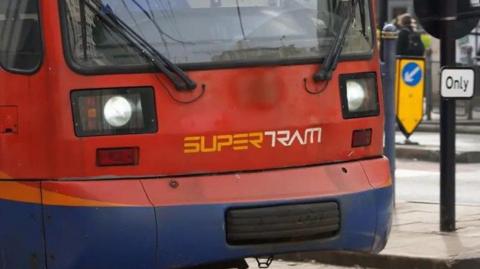 A red tram makes its way down a city street. The word 'Supertram' is emblazoned across the front