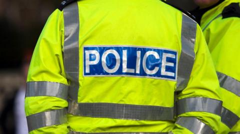 The back of a hi-vis yellow police jacket with the word Police in white lettering on a blue background
