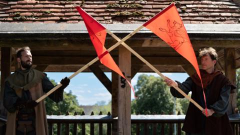 Two men in historical costumes holding an orange flag on top of Bedford's Castle Mound