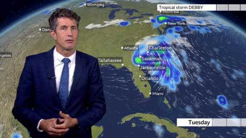 Chris Fawkes stands in front of a weather map of the US