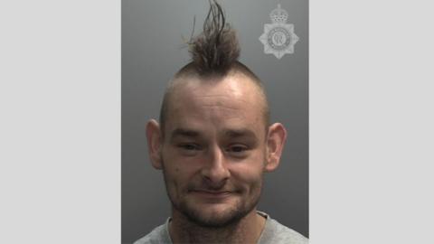A man with brown hair in a Mohican style in a police custody photo, with a Humberside Police crest watermark on it.