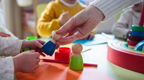 Young children playing with painted wooden toys at a table. 