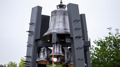 A big bell with HOPE cast on it held up by four steel supports