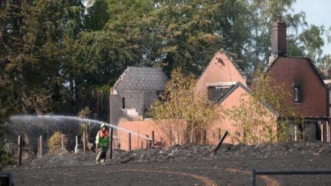 Firefighters damp down the charred remains of a field close to burnt houses following a huge blaze in Stourbridge, in the West Midlands