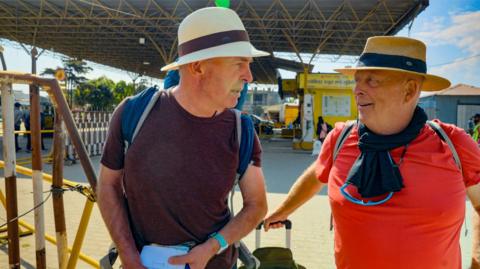 Brian and Melvyn wear hats and backpacks while standing next to each other.