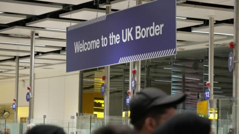 A UK border sign in an indoor area with unidentifiable people beneath it