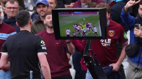 Referee Chris Kavanagh watches the VAR replay before disallowing a goal from Callum Wilson of West Ham United after a foul on Arsenal goalkeeper David Raya