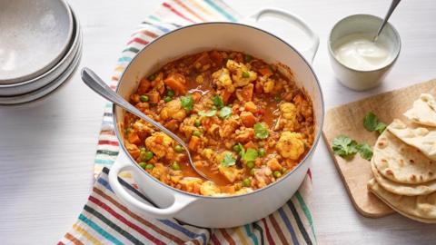 A large pot containing vegetable and lentil curry with visible bits of cauliflower, garnished with coriander and served with naan breads.