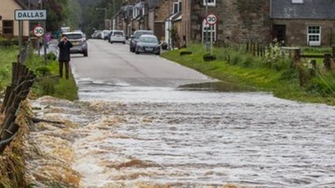 Water rushes over the road out of Dallas in Moray