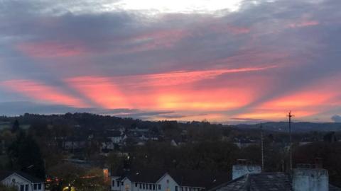 Yellow and red slices of light arc up from the horizon over a sea of houses and rooftops in the foregound.