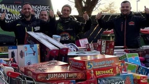 Four men next to Christmas presents