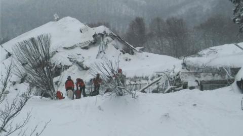 Members of Lazio's Alpine and Speleological Rescue Team stand in front of the Hotel Rigopiano in Farindola, central Italy